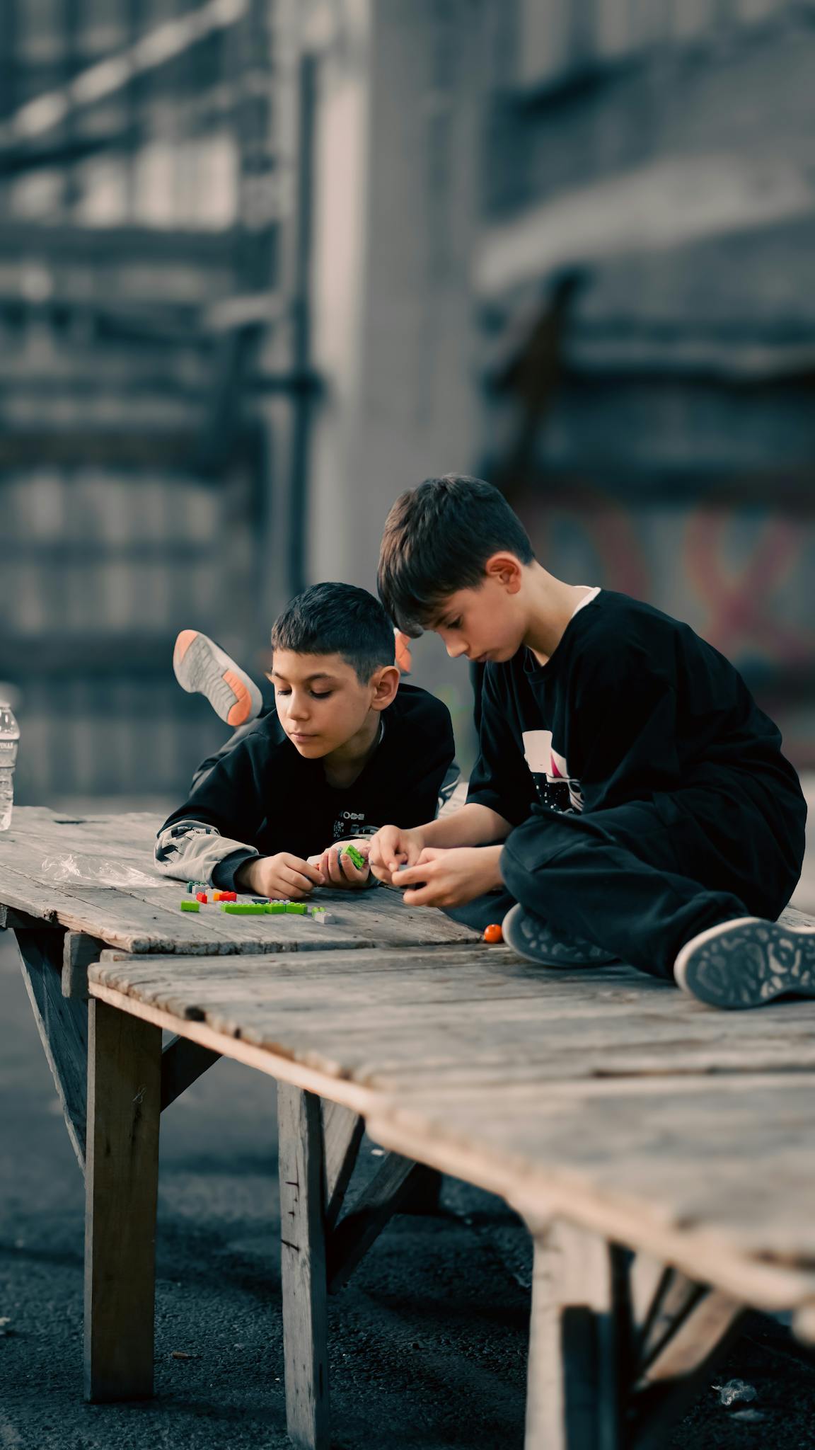 Two boys playing with colorful blocks on a wooden platform outdoors, in an urban setting.